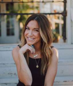 Smiling woman with highlighted hair wearing a black top and necklace.