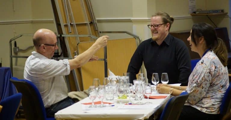 People enjoying a cheese & wine evening, laughing around a table with wine glasses.
