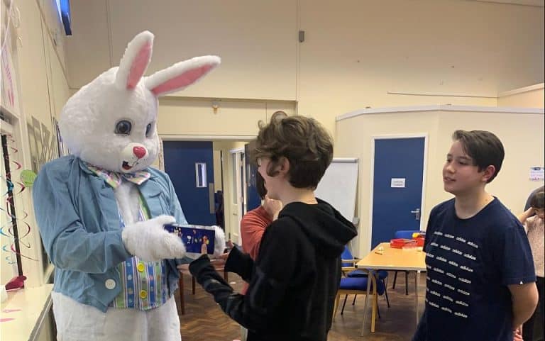 Signing Easter Bunny presents a gift to a child in a room full of people.
