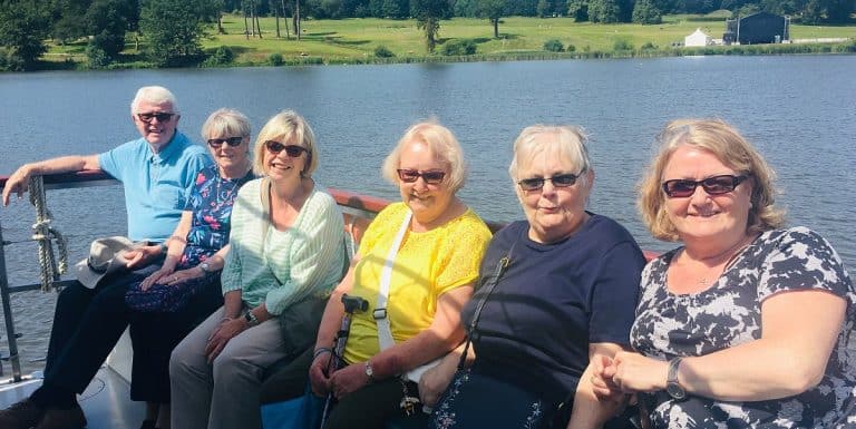 Group of seniors enjoying a boat ride at Trentham Gardens, smiling and wearing sunglasses.
