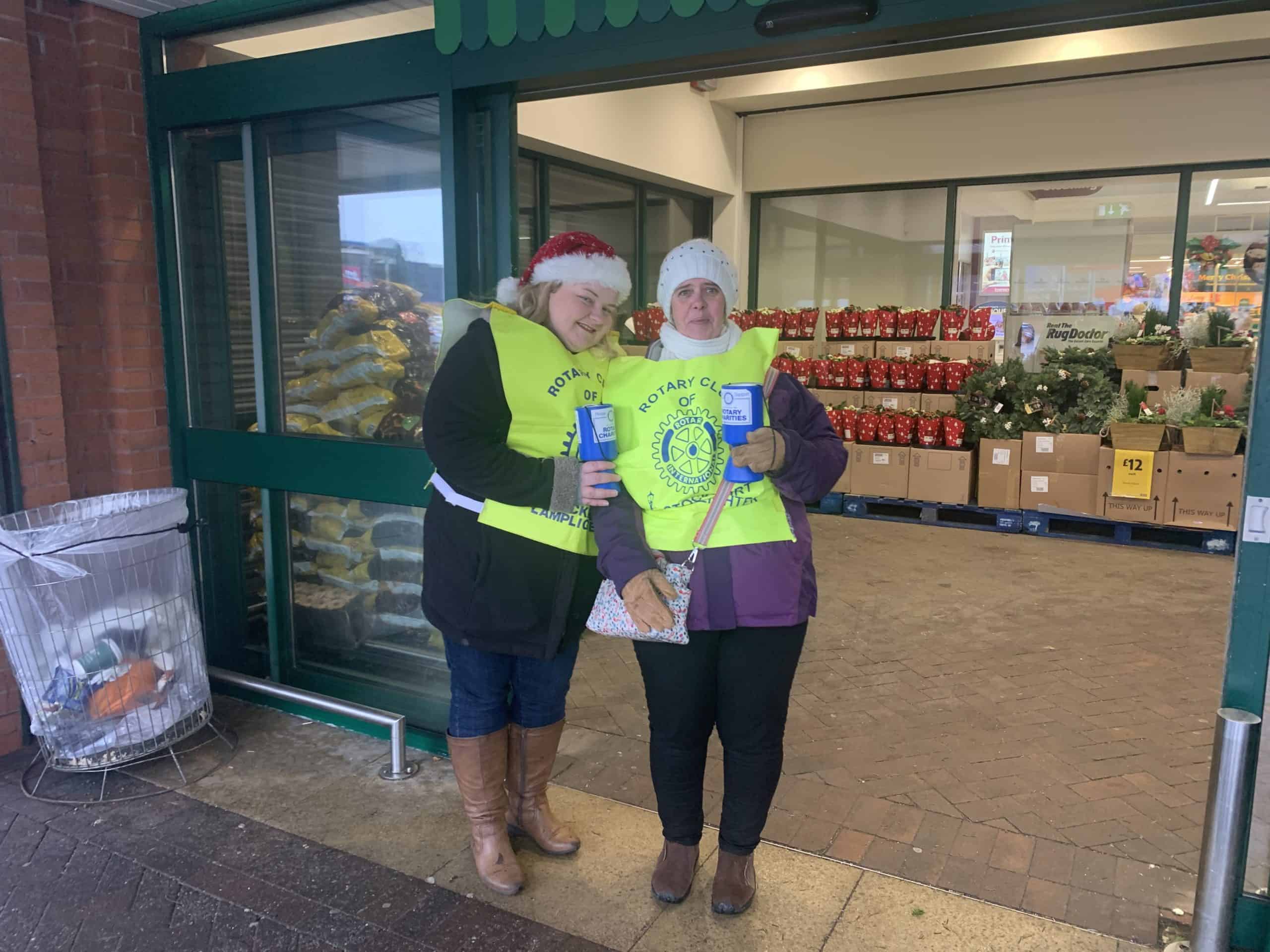 Two women in Rotary Club vests collect donations outside a store.