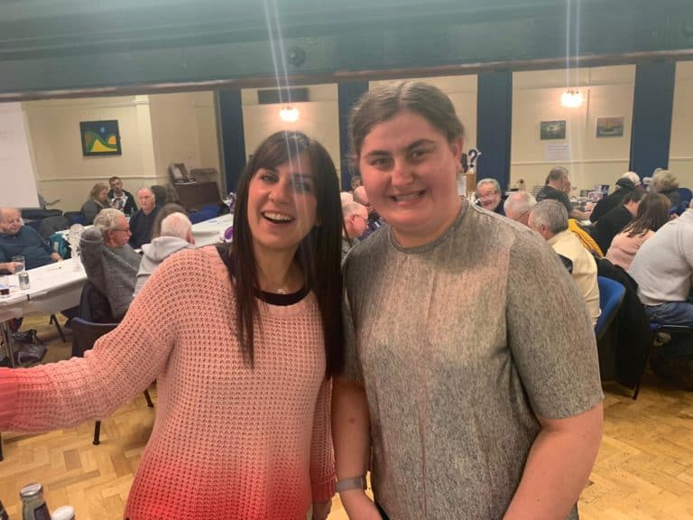 Two smiling women pose at a lively quiz night event.