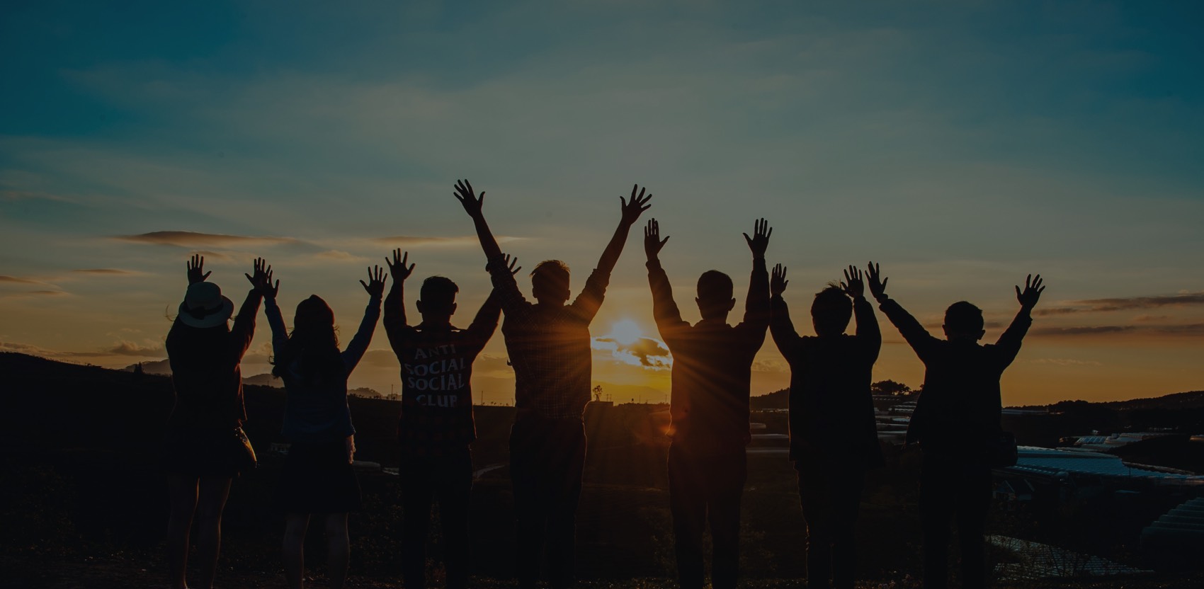 Silhouetted group raising hands at sunset. Volunteer spirit and teamwork.