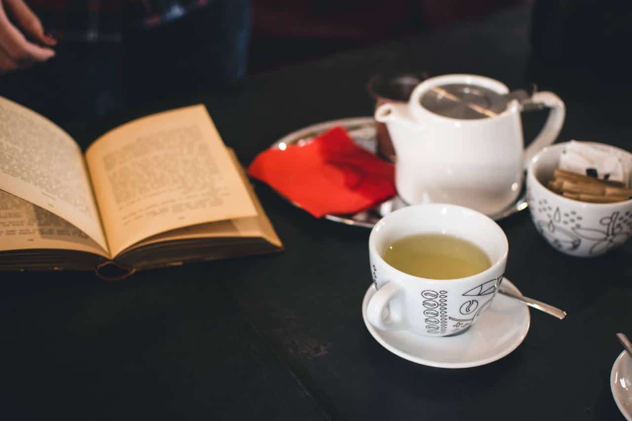 Open book, cup of tea, and teapot on a dark table, creating a cozy reading atmosphere.