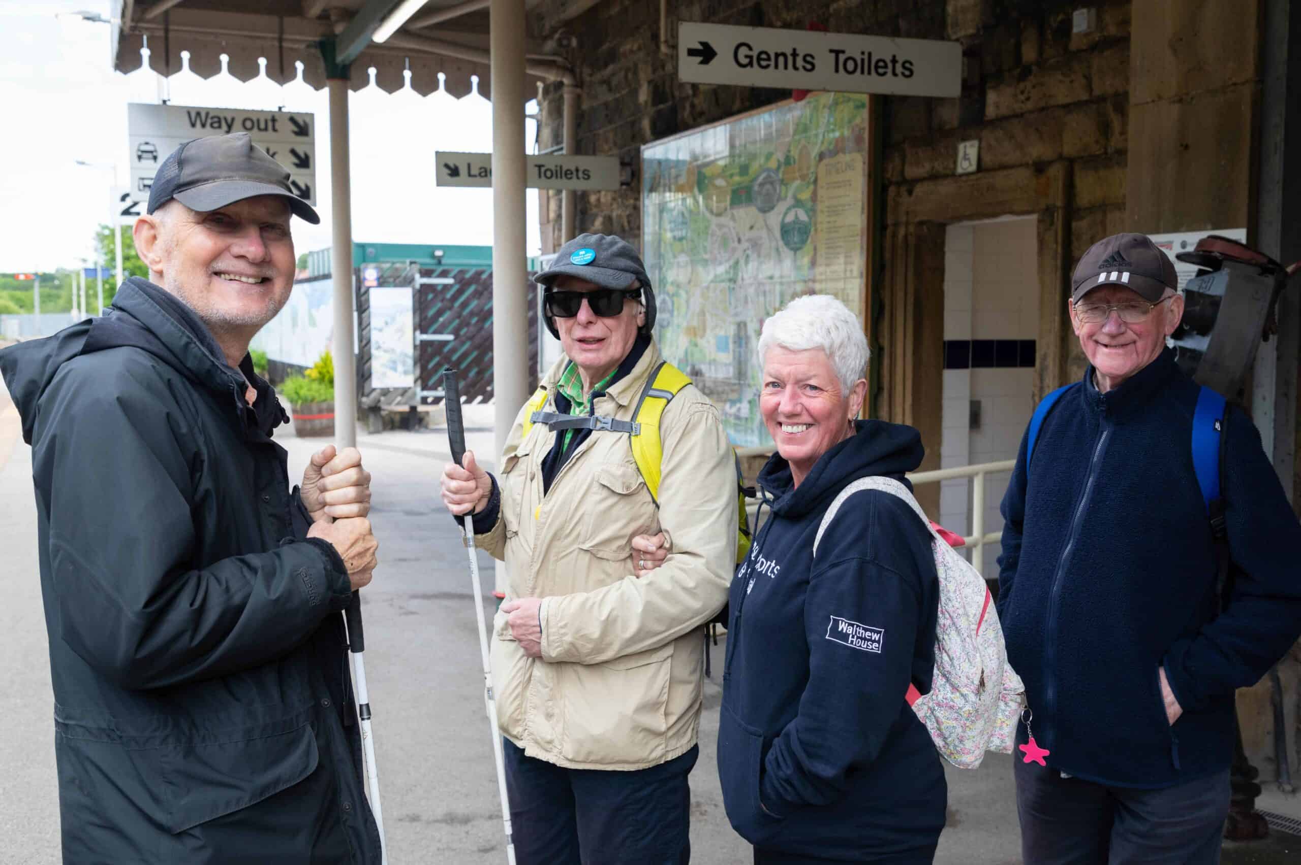 Group of adults stood on a train station platform.