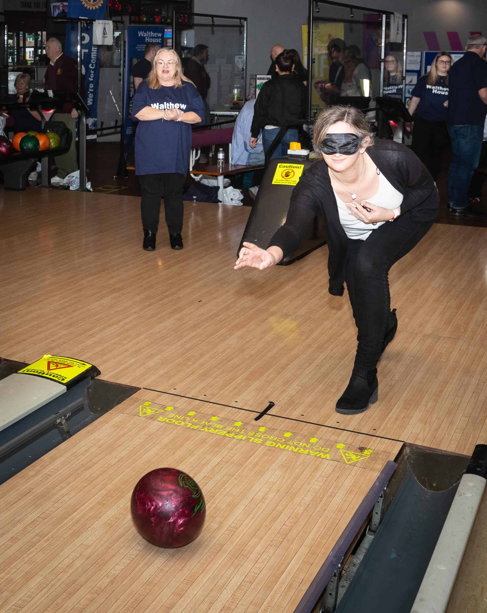 Woman bowling whilst wearing a blindfold.
