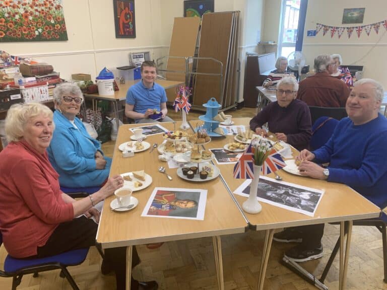 Walthew's May newsletter: Group enjoying a tea party with Union Jack decorations and treats.