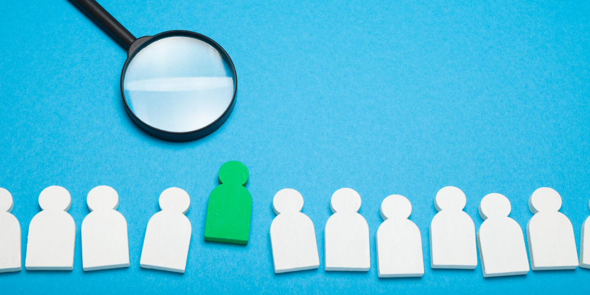 Magnifying glass over a green figure standing out from white figures; vacancy concept.