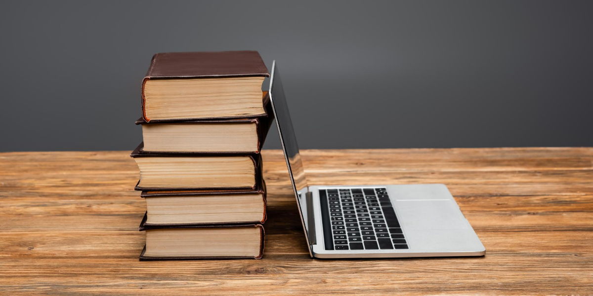 Stack of books next to a laptop on a wooden desk.
