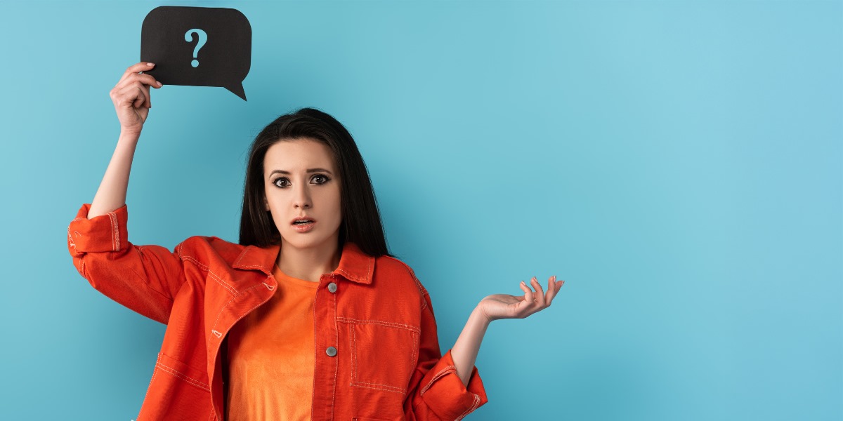 Confused woman holding question mark sign against blue background