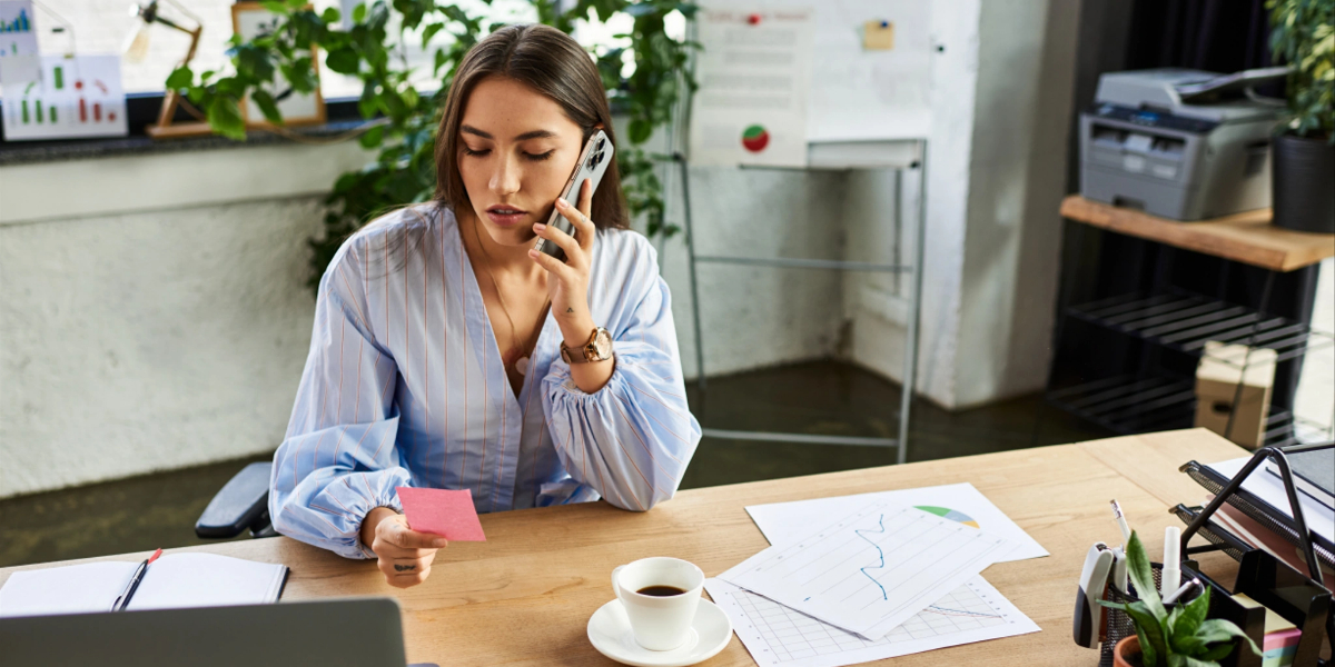 Woman on phone at desk with Advocacy & Information charts, coffee, and laptop.