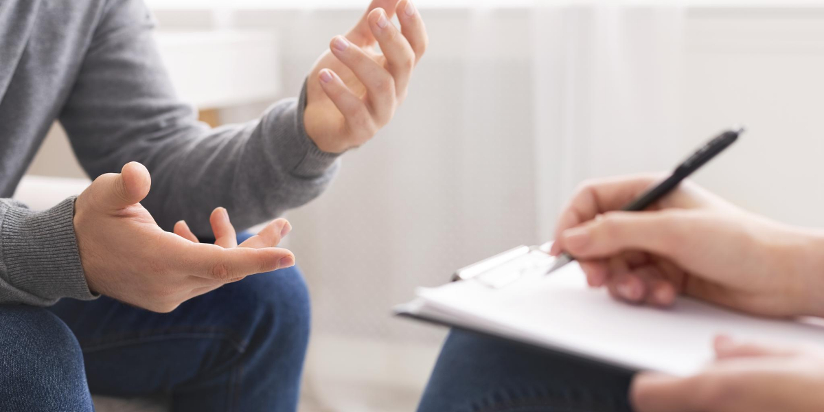 Person gesturing while talking to a counselor who is taking notes on a clipboard.