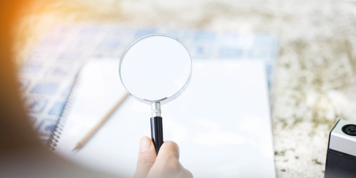 Hand holding magnifying glass over notebook; resource center research