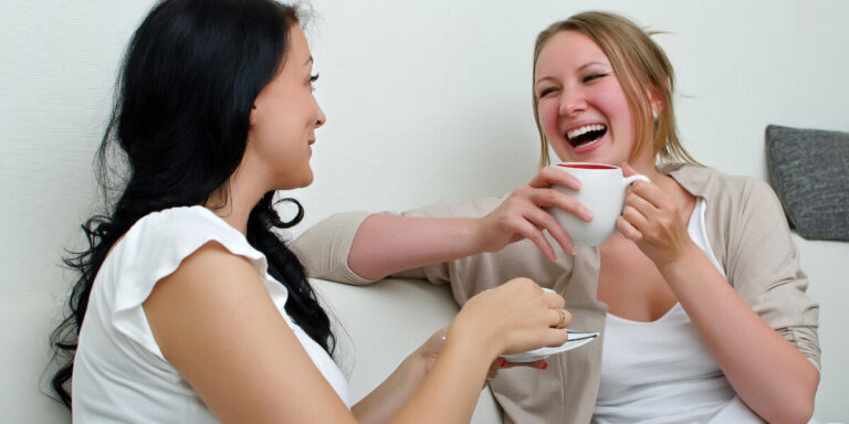 Two women enjoy tea together, laughing and chatting. Supporting friendships for sight loss.