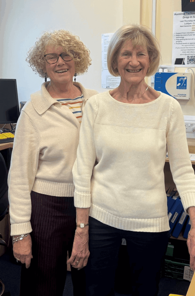 Two women standing and smiling our resource centre. Both are wearing light coloured tops and are smiling.