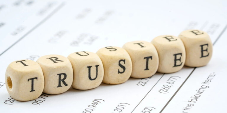 Wooden blocks spelling "TRUSTEE" on financial documents.