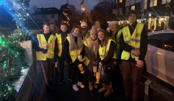 Group of volunteers in high-visibility jackets collecting donations at nighttime