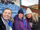 Three women wearing volunteer lanyards at a stadium. 