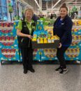 Two ASDA employees stocking Easter candy displays at a self-checkout area in a grocery store.