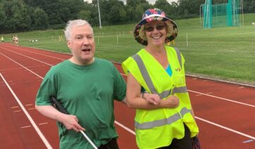 Ben Man walking with a long cane, linking arms with a woman in a hi-vis jacket.