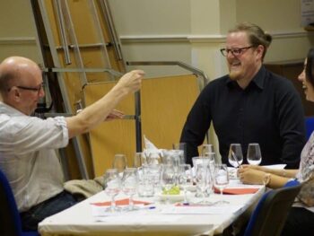People enjoying a cheese & wine evening, laughing around a table with wine glasses.