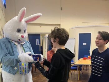 Signing Easter Bunny presents a gift to a child in a room full of people.