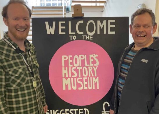Two men stand smiling beside a 