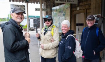 Group of adults stood on a train station platform.