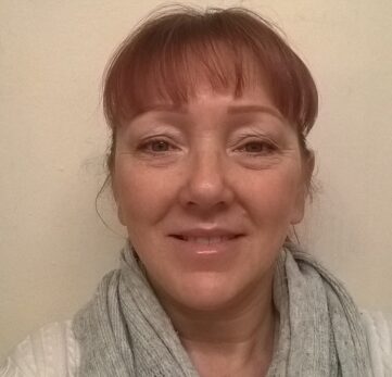 Woman with red hair and a gray scarf smiles at the camera.