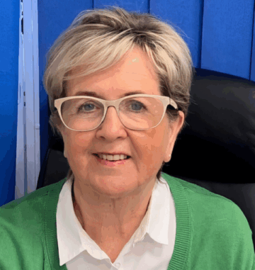 Mature woman with glasses and short blonde hair smiling at the camera.