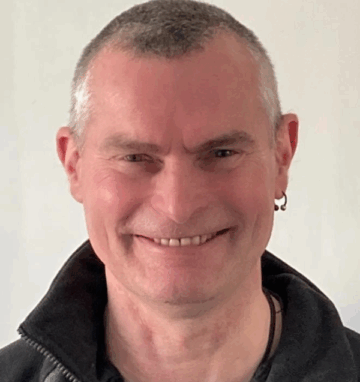 Smiling middle-aged man with short grey hair and an earring, wearing a black jacket.