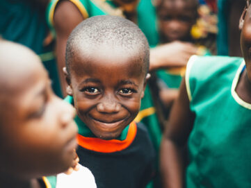 Smiling African child in black and orange shirt, part of community projects.