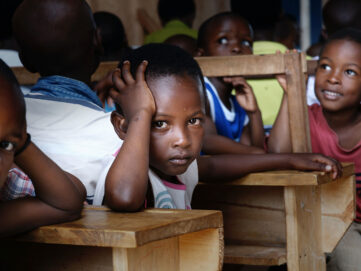Young students in a classroom, one resting head on hand, looking thoughtful.