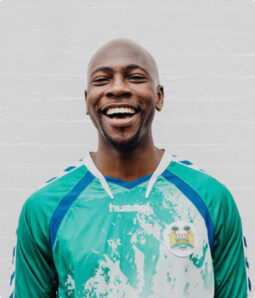 Smiling Black man in a green and blue soccer jersey.